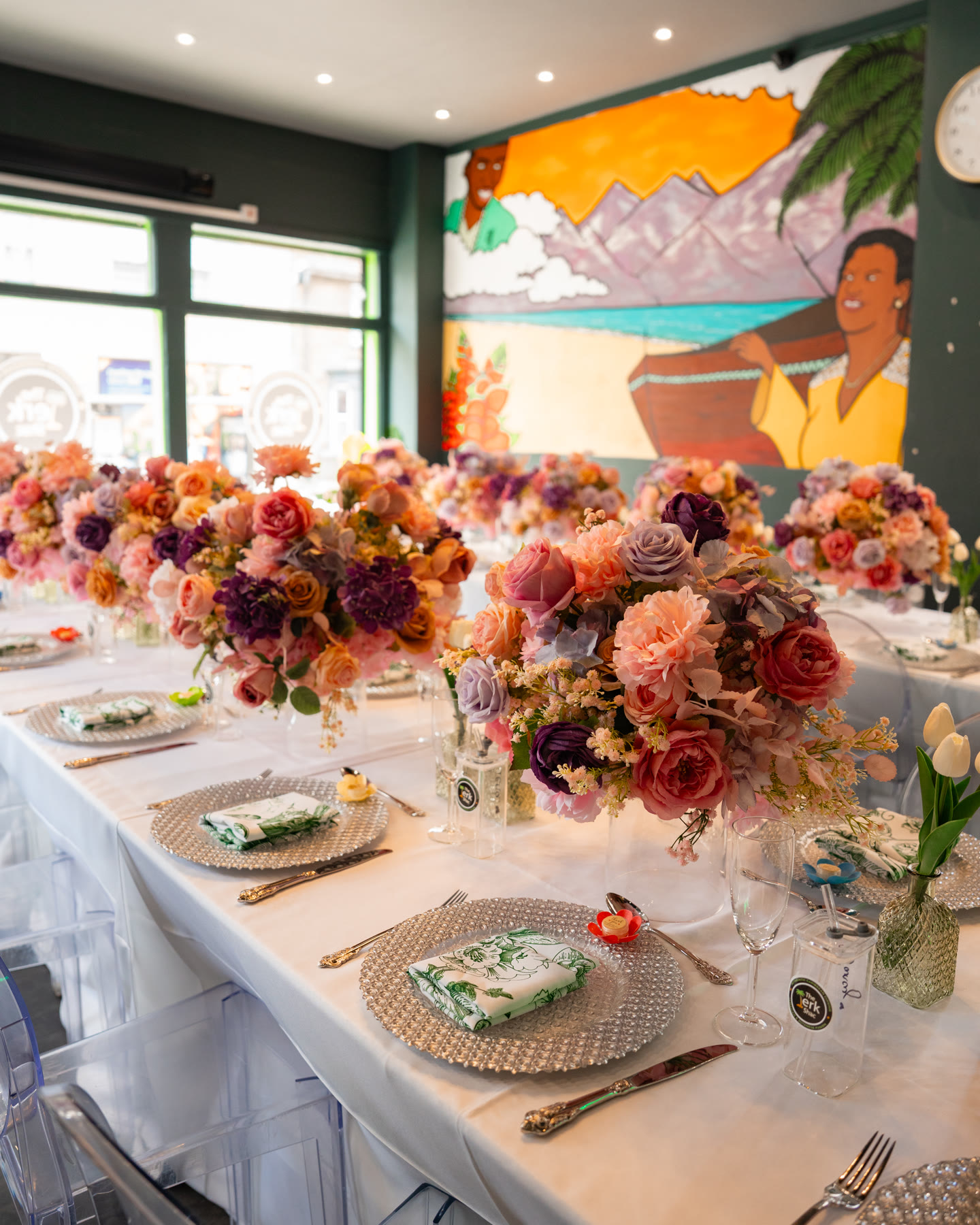 A private dining table surrounded by flowers beneath The Jerk Shac mural